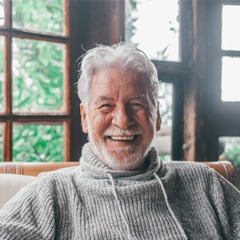 Senior man in grey sweater sitting and smiling at home