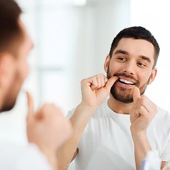 man flossing teeth in bathroom mirror