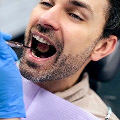 Gloved hand holding dental mirror in man’s mouth during exam