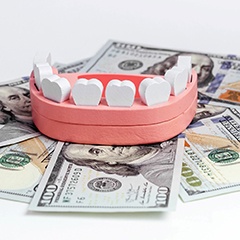 a wooden model of a mouth with teeth sitting on top of money
