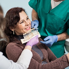a person having their teeth color-matched at the dental office looking into a mirror in their hand