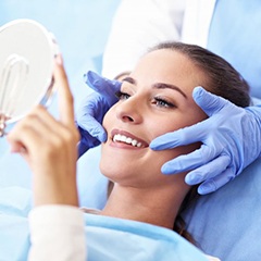 woman sitting in dental chair and smiling at hand mirror 
