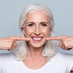 Woman with grey hair smiling while pointing to her teeth