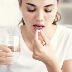 woman taking a pill with a glass of water