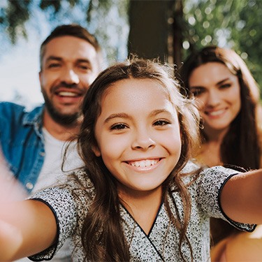 Young daughter taking selfie with parents.