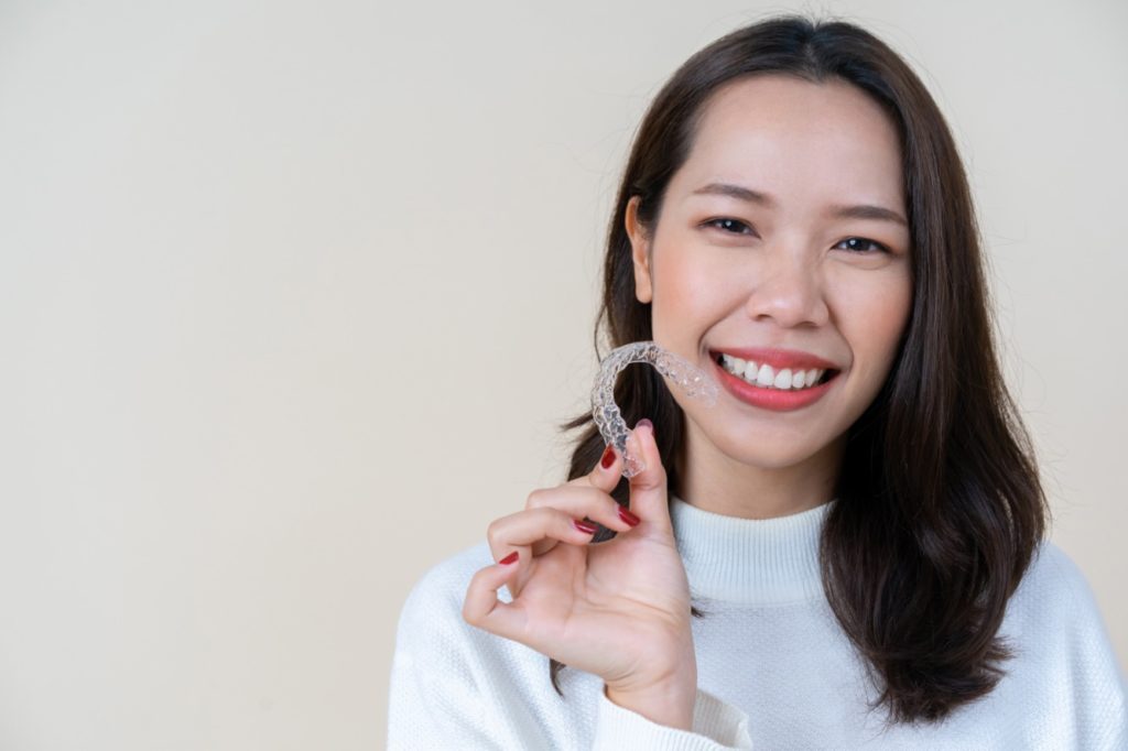 Woman being treated with Invisalign in Sunnyvale is holding a clear aligner tray