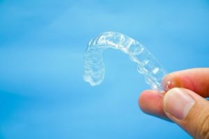 A clear aligner being held up in front of a blue background