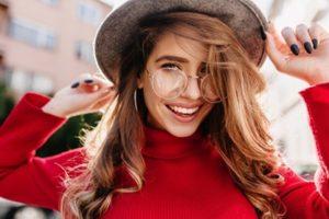Young woman wearing a hat, glasses, and a red sweater smiling.