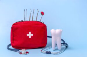 Large toy tooth next to a red cross emergency bag holding dental instruments