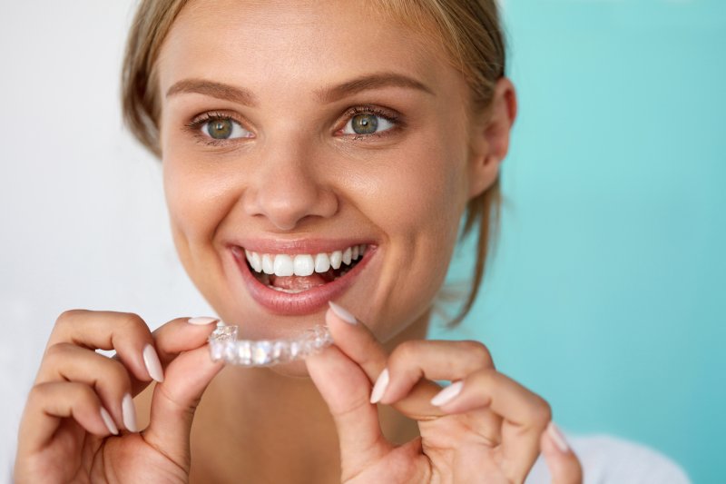 Woman holding up her Invisalign aligner with a smile