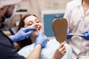 Dentist performing cosmetic dentistry on patient while she looks into mirror. 