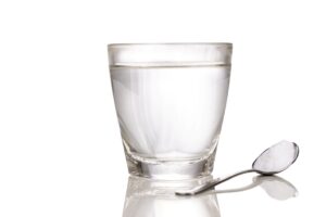 Glass of water next to spoon full of salt on reflective surface